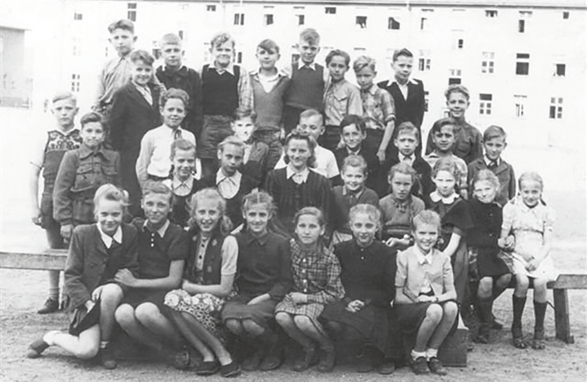 Kara bēgļi. Lībekas latviešu pamatskolas 5. klases kopbilde 1948. gada vasaras beigās. Vaira pirmajā rindā pirmā no labās, fonā — bēgļu kazarmas. Karš pilnīgi mainīja ģimenes likteni, liekot doties bēgļu gaitās un nesot traģisku zaudējumu — tikai dažas nedēļas pēc Rīgas pamešanas 1945. gada janvārī briesmīgajos apstākļos Vācijā saslima un nomira Vairas mazā māsa Mārīte. Foto no privātā arhīva