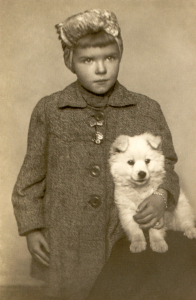 1944. gada sākumā Rīgā. Ar špicu sugas kucēnu Pupsi. «Lakats sedz kailu galvu, jo D vitamīna trūkuma dēļ veseliem laukumiem bija izkrituši mati un pārējie noskūti.» Foto no privātā arhīva