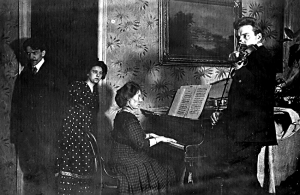 Ivandes Kaijas māsas ar saviem ciemiņiem Melderu-Milleru Altonavas ielas dzīvoklī ap 1908./1909. gadu. No kreisās — Teodors Hermanovskis, Paulīne Millere, Ella Millere (pie klavierēm), ar vijoli — Maksimilians Robežgruntnieks. Foto no Marijas Ņesterovas privātā arhīva