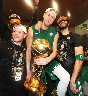 Kristaps Porziņģis ar NBA čempiona trofeju. Blakus komandas biedrs Džeisons Teitums (pa labi) un rehabilitācijas vadītājs Stīvs Mounts
