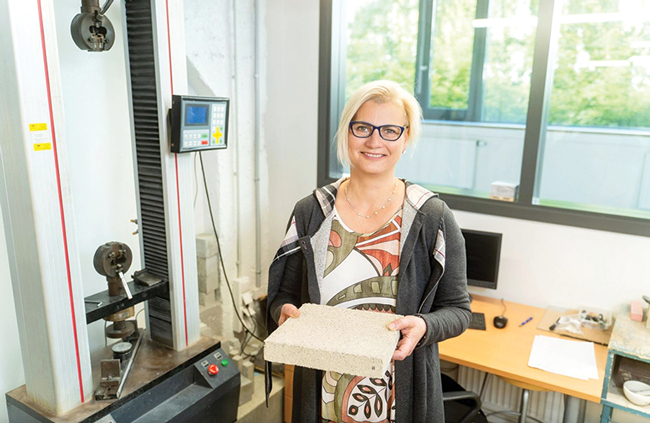 RTU Būvniecības un mašīnzinību fakultātes tenūrprofesore Diāna Bajāre ar eksperimentālu plāksni, kas tapusi sadarbībā ar koka ēveļskaidu plātņu ražotāju Cewood. Kā izejvielas izmantoti ražošanas atlikumi un blakusprodukti, papildinot tos ar dabīgām izejvielām. Publicitātes foto