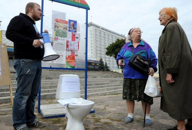 Svētdien Baltkrievijā paredzētās parlamenta vēlēšanas boikotēs divas lielākās opozīcijas partijas. Attēlā: opozīcijas pārstāvis pie savdabīgas instalācijas ar klozetpodu aicina boikotēt vēlēšanas. Foto: AFP/LETA