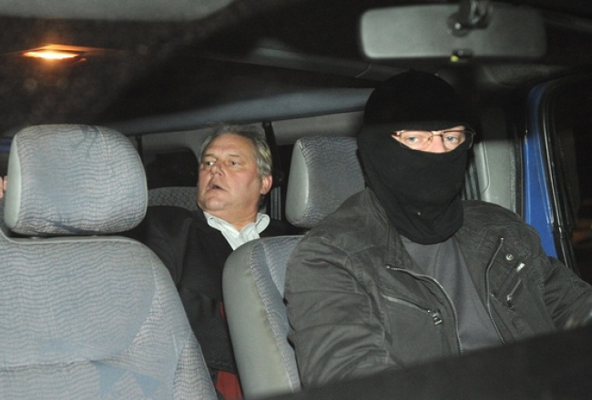 Dzintars Jaundžeikars kopā ar KNAB darbinieku tiek konvojēts uz apcietinājuma vietu. Foto: Lita Krone, LETA