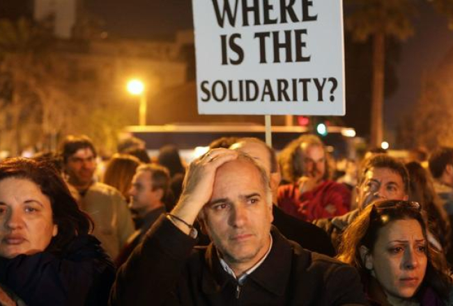 Ceturtdienas vakarā daudz ļaužu piedalījās demonstrācijā pie Kipras valdības ēkas. "Kur ir solidaritāte?" vaicā plakātā bēdu sagrautie kiprieši. Foto: AFP/LETA