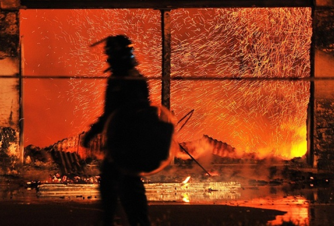 Policists pie degošās rūpnīcas Londonas piepilsētā. Foto: AFP/LETA