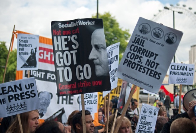 Protestētāji Londonā pauž attieksmi pret Mērdoka medijiem. Foto: AFP/LETA