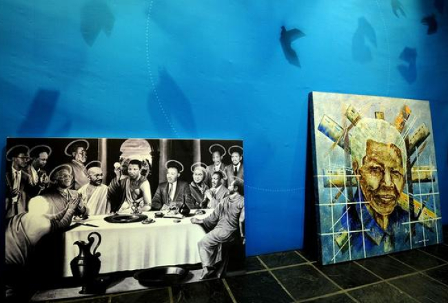 Izstādē Johannesburgā - glezna "Svētais vakarēdiens" (pa kreisi), ko radījis mākslinieks Dans Saimons, un "Mandela globālajā ikonā" - mākslinieks Daniels Mosako. Foto: AFP/LETA