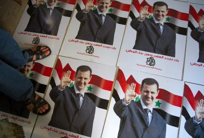 Kāds vīrs stāv uz plakātiem ar Sīrijas prezidenta Bašara al Asada portretu. Foto: AFP/LETA