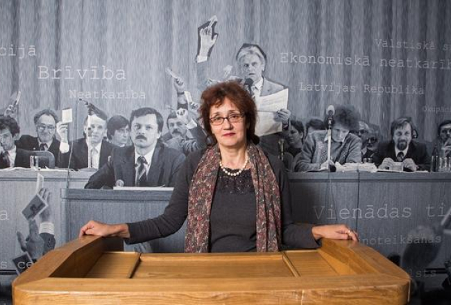 LTF muzeja vadītāja Meldra Usenko pie vēsturiskās Kongresu nama tribīnes. Viņai aizmugurē palielināta fotogrāfija no LTF dibināšanas kongresa prezidija, kas atradās uz Kongresu nama skatuves. Foto: Andrejs Terentjevs, F64