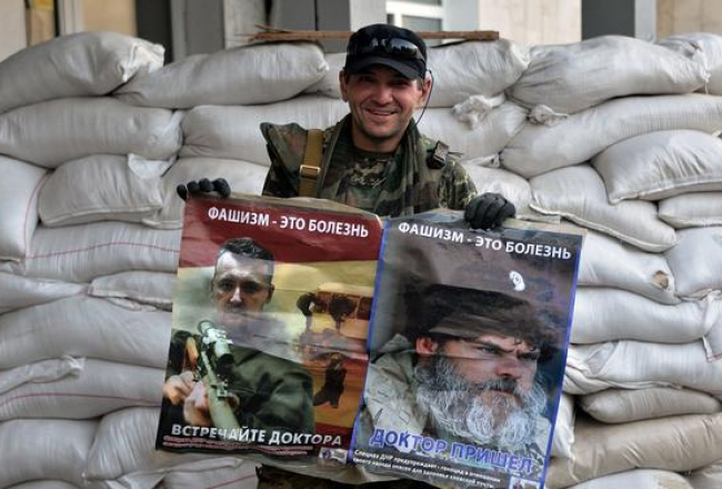 Prokrievisko separātistu kaujinieks šogad jūlijā Donbasā rokās tur Krievijas propagandas plakātus, kuros redzams teroristu vadonis Igors Girkins un kāds bārdainis. Saukļi uz plakātiem vēsta: "Fašisms - tā ir slimība. Sagaidiet ārstu!". Foto: ITAR-TASS/LETA