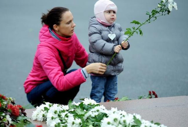 Sieviete ar bērnu noliek ziedus lielveikala jumta sabrukšanas upuriem. Foto: Evija Trifanova, LETA