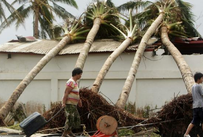 Filipīnieši iet garām taifūna izgāztajām palmām. Foto: EPA/LETA