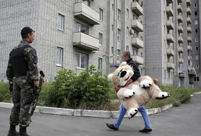Karš un miers. Ukrainas armijas karavīrs noskatās, kā Austrumukrainas Avdejevkas pilsētiņas iedzīvotājs dodas uz mājām. Foto: AFP/LETA