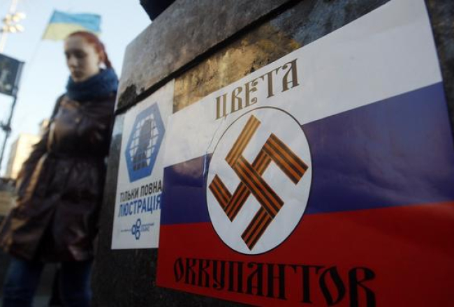 Kijevas Neatkarības laukumā pielīmēts plakāts, kas attēlo Krievijas karoga krāsas, uz kurām ir nacistu svastika. Uzraksts vēsta: okupantu krāsas. Foto: AFP/LETA