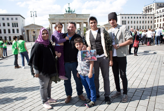 Sīriešu bēgļu ģimene Berlīnē pie Brandenburgas vārtiem pozē: no kreisās - Nada, Noor, Laith Majid Al-Amirij, Taha, Ahmeds un Mustafa. Foto: EPA/LETA