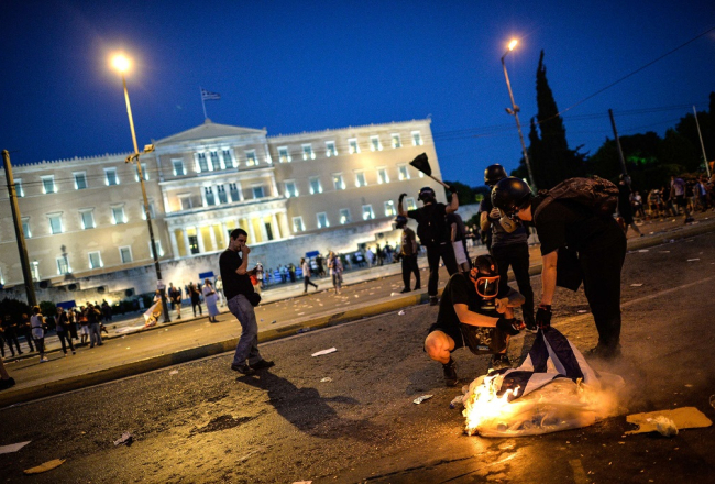 Protestētāji pie Grieķijas parlamenta ēkas Atēnās pagājušajā naktī, kad apsprieda reformu plānu. Foto: AFP/LETA