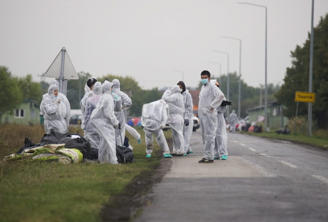 Brīvprātīgie aizsardzības tērpos savāc atkritumus, kas palikuši pēc migrantiem, kad tie šķērsoja Serbijas un Horvātijas robežu. Foto: EPA/LETA