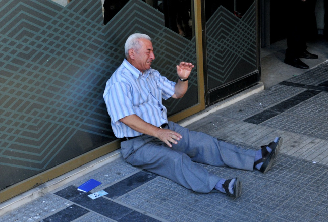 Grieķu pensionārs Giorgoss Hatzifotiadis sēž pie bankas un raud, uzzinājis, ka atļauts izņemt tikai 120 eiro no pensijas. Foto: AFP/LETA