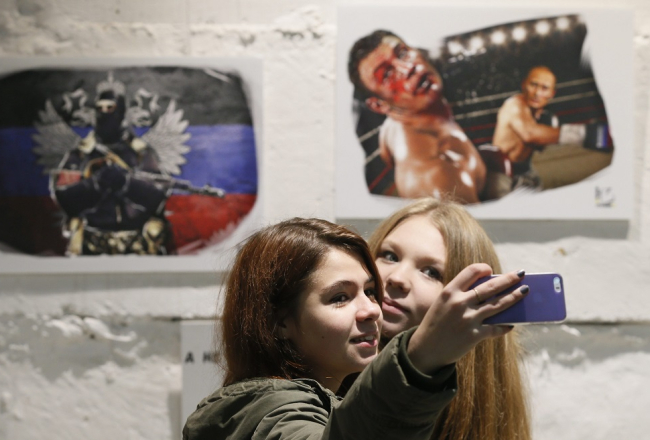 Propaganda darbībā - pērnruden izstādē Maskavā meitenes fotografējas - fonā Putina "spēku" slavinoši "mākslas darbi": Putins boksā uzvar ukraini Vitāliju Kļičko. Foto: EPA/LETA