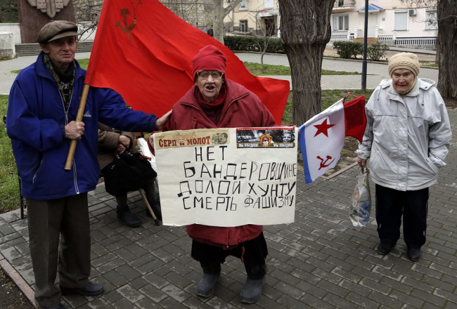 Nemainīgā pārliecība arī šodien Krievijas Ukrainai atņemtajā Sevastopolē - padomju laikus piedzīvojušie tur plakātu ar uzrakstu: "Nē baderoviešiem, nost ar huntu, nāvi fašismam!". Foto: AFP/LETA