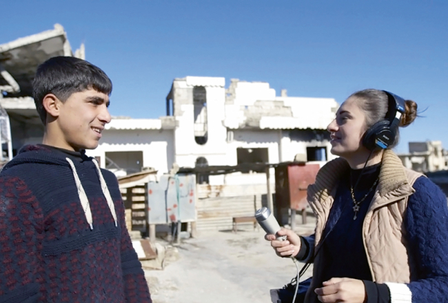 Kadrs no Radio Kobane. 20 gadus vecā Dilovana Kiko vada radio pārraides smagi izpostītajā Sīrijas pilsētiņā Kobanē.