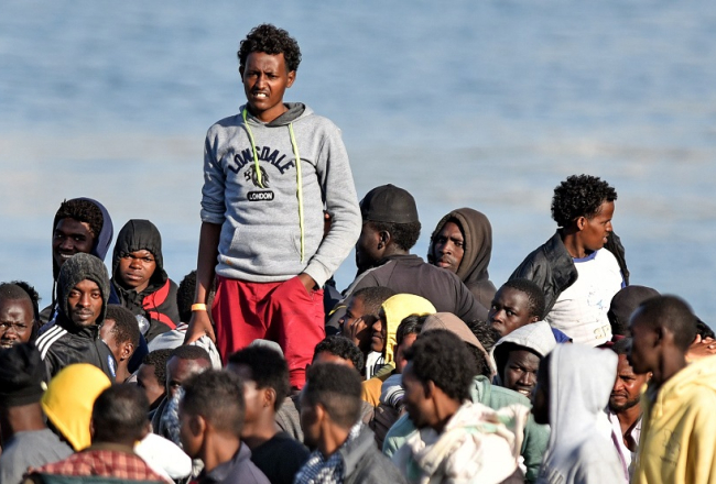 Migranti krasta apsardzes kuģī gaida, kad varēs izkāpt Itālijas krastā. Foto: AFP/LETA