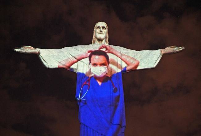 Slavenā Jēzus Kristus statuja Riodežaneiro Lieldienās tika izgaismota mediķa virsvalkā. Ārsti fotgrafējās uz tās fona. Foto: AFP/Scanpix/LETA