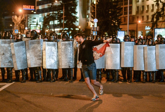 Pēc vēlēšanām Minskā sākās masveida opozīcijas miermīlīgi protesti pret vēlēšanu rezultātu viltošanu. Protestētājs ar Baltkrievijas karogu pirms OMON vienības kaujiniekiem, kuriem bija dota pavēle Minskā ieviest kārtību. Foto: EPA/Scanpix