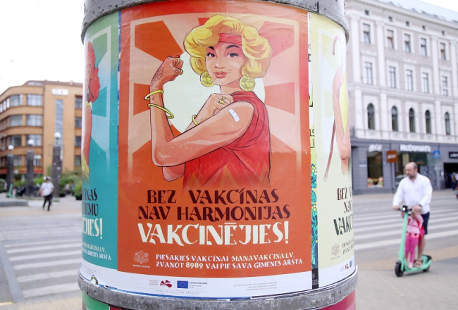 Vakcinācijas pret Covid-19 vides plakāti uz reklāmstaba. Foto: Paula Čurkste, LETA