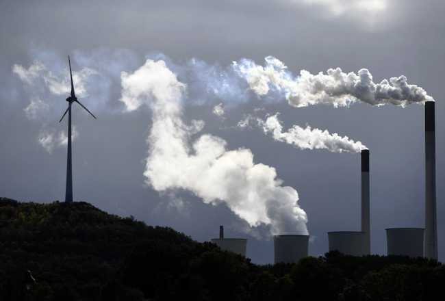 Dūmi no globālās energoapgādes uzņēmuma "Uniper" ogļu spēkstacijas līdzās vēja turbīnai Vācijas pilsētā Gelzenkirhenē 2019. gadā. Foto - INA FASSBENDER, AFP