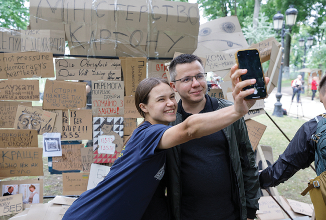 Jaunieši Kijivā pozē pie simboliskas sienas ar plakātiem, kuri tika izmantoti protestos pret pretkorupcijas iestāžu neatkarības likvidēšanu.