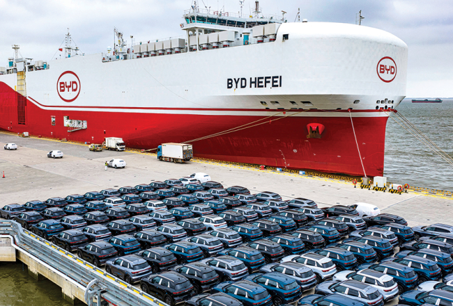 BYD elektroauto pirms iekraušanas kravas kuģī ostā pie Šanhajas.