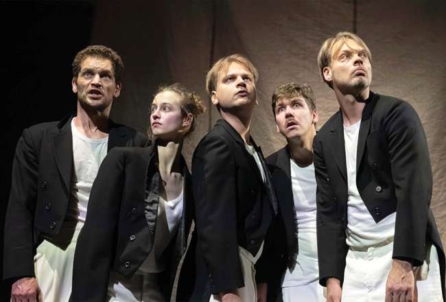Melnās frakās tērpušies, izrādes aktieri — Edgars Ozoliņš, Polina Čerņenoka, Kārlis Ērglis, Hugo Puriņš un Gatis Maliks — sarunājas kā tās caunas, kuras seši mazi bundzenieki padarījuši par cepurēm. Foto — Aigars Hibneris