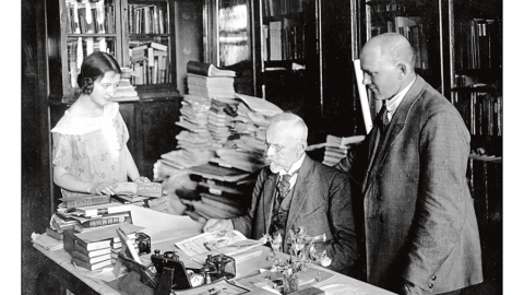 Jānis Misiņš (vidū) ar audžumeitu Hermīni un bibliofilu Fišeru savā mājas bibliotēkā Rīgā. 20. gadsimta 20. gadi. Fotogrāfs nezināms. LU bibliotēkas Misiņa bibliotēkas krājums