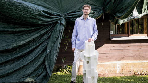 Arturs ar paša atlieto vecvecmāmiņas Martas Liepiņas-Skulmes skulptūras repliku. Skulmju mājās pašlaik maina jumtu, tāpēc ietīta plēvēs.