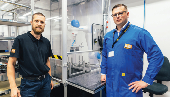 Produktivitātes rādītājus HansaMatrix Ventspils ražotnē uzlabo, izmantojot arī robotu roku darbu, rāda Edžus Siliņš (pa kreisi) un Dāvis Šnikvalds.