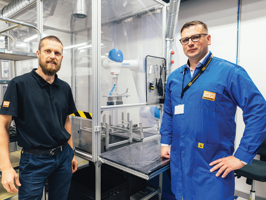 Produktivitātes rādītājus HansaMatrix Ventspils ražotnē uzlabo, izmantojot arī robotu roku darbu, rāda Edžus Siliņš (pa kreisi) un Dāvis Šnikvalds.