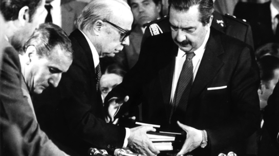 1984. gada 20. septembris. Argentīnas Nacionālās personu pazušanas komisijas (CONADEP) prezidents rakstnieks Ernesto Sabato (no kreisās) pasniedz valsts prezidentam Raulam Alfonsīnam komisijas gala ziņojumu. To izdeva arī grāmatā Nunca mas (Nekad vairs).
Argentīnas Nacionālā ģenerālarhīva krājums