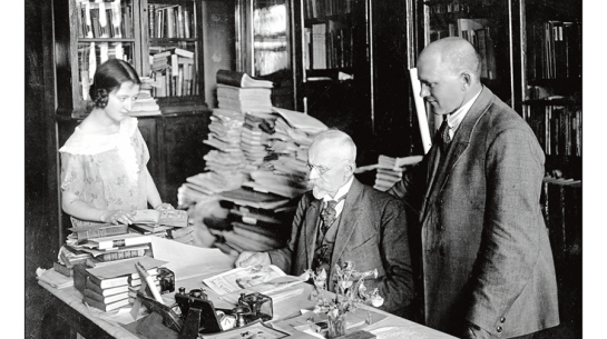 Jānis Misiņš (vidū) ar audžumeitu Hermīni un bibliofilu Fišeru savā mājas bibliotēkā Rīgā. 20. gadsimta 20. gadi. Fotogrāfs nezināms. LU bibliotēkas Misiņa bibliotēkas krājums