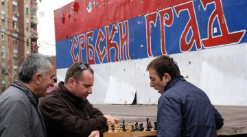Vīri spēlē šahu Kosovas pilsētā Mitrovicā. Sienas grafiti uzraksts vēsta, ka šī ir serbu pilsēta. Foto: AFP/LETA