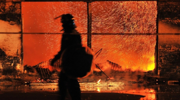 Policists pie degošās rūpnīcas Londonas piepilsētā. Foto: AFP/LETA