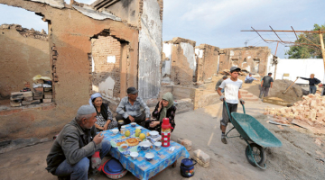 Uzbeku ģimene pie savas nopostītās mājas Ošā. Foto — AFP/LETA