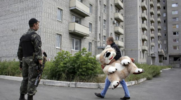 Karš un miers. Ukrainas armijas karavīrs noskatās, kā Austrumukrainas Avdejevkas pilsētiņas iedzīvotājs dodas uz mājām. Foto: AFP/LETA