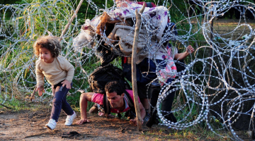 Nelegālie imigranti pie Roszke ciema uz Ungārijas-Serbijas robežas pa caurumu dzeloņdrāšu žogā šķērso robežu. Foto: AFP/LETA