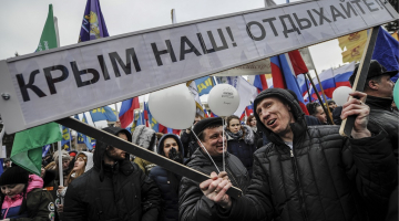 Sajūsminātie krievi Krimas okupācijas gadadienas svinībās Maskavas Sarkanajā laukumā. Uzraksts vēsta - Krima ir mūsu - atpūtieties! Foto: ITAR-TASS/LETA