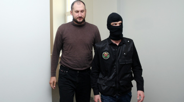 Viens no aizturētajiem Krievijas pilsoņiem Aleksandrs Kurkins, kurš nelikumīgi bija iekļuvis Ādažu militārajā bāzē un pie kura atrastas skrejlapas angļu valodā, tiek konvojēts uz Rīgas pilsētas Vidzemes priekšpilsētas tiesas sēdi, kurā lems par drošibas līdzekļa piemērošanu. Foto: Ieva Čīka, LETA