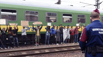 Migranti Ungārijā pie vilciena, no kura atteicās izkāpt un doties uz patvēruma meklētāju centru. Migranti improvizētos plakātos tur uzrakstus, ka vēlas doties uz Vāciju, nevis palikt Ungārijā. Foto: EPA/LETA