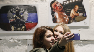 Propaganda darbībā - pērnruden izstādē Maskavā meitenes fotografējas - fonā Putina "spēku" slavinoši "mākslas darbi": Putins boksā uzvar ukraini Vitāliju Kļičko. Foto: EPA/LETA
