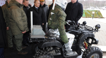 Krievijas prezidents Vladimirs Putins (centrā) un Dmitrijs Rogozins (pa labi) iepazīstas ar militāristu jaunumiem - robotu-karotāju, kas spēj braukt arī ar kvadraciklu. Foto: ITAR-TASS/LETA