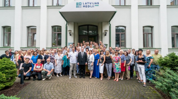 Izdevniecības darbinieki pie ēkas ar jauno logo. Publicitātes foto